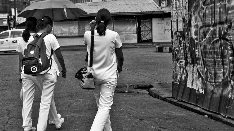 A photograph of three people in white scrubs walking away from the camera and towards a building.